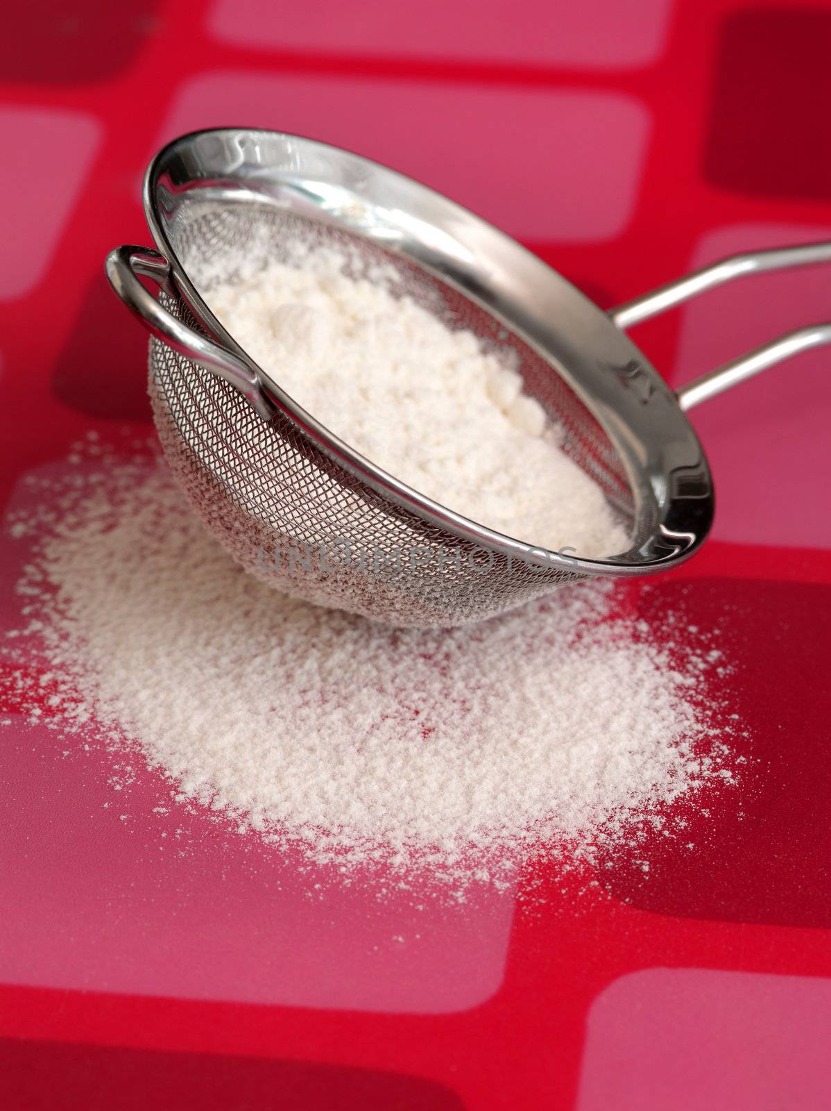 Macro photo of a sifter and flour on a pink retro countertop.