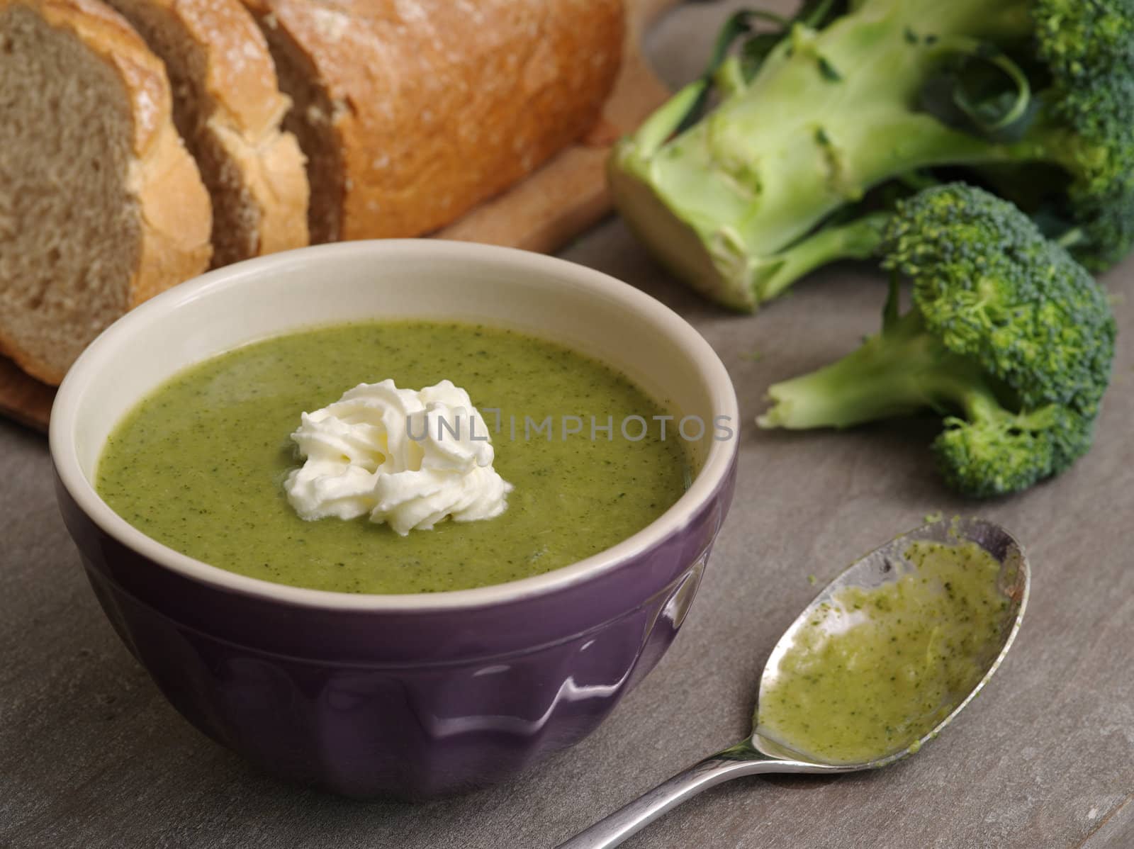 Photo of broccoli soup with a loaf of bread in the background.
