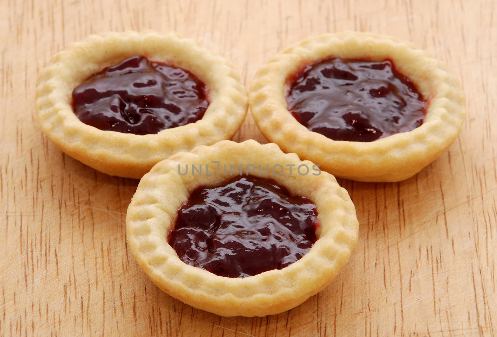 Three tasty jam tarts sitting on a wooden table
