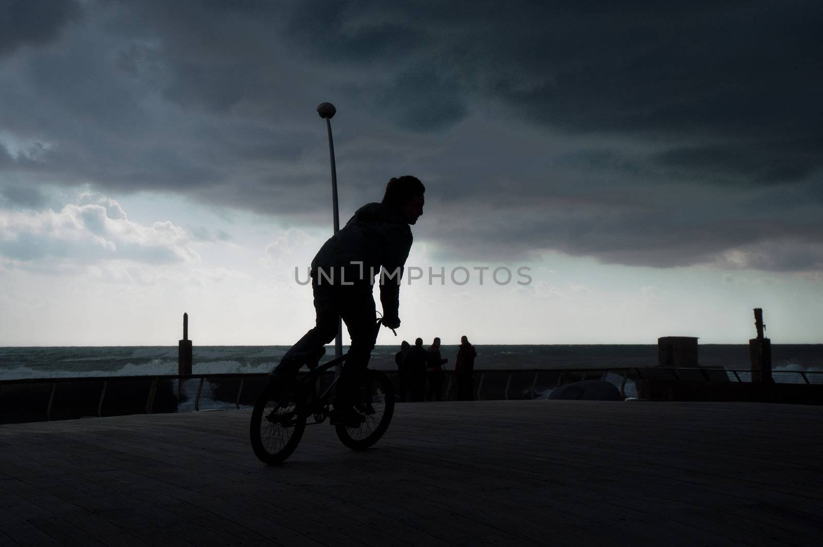 Teenager rides a bicycle along the seafront .