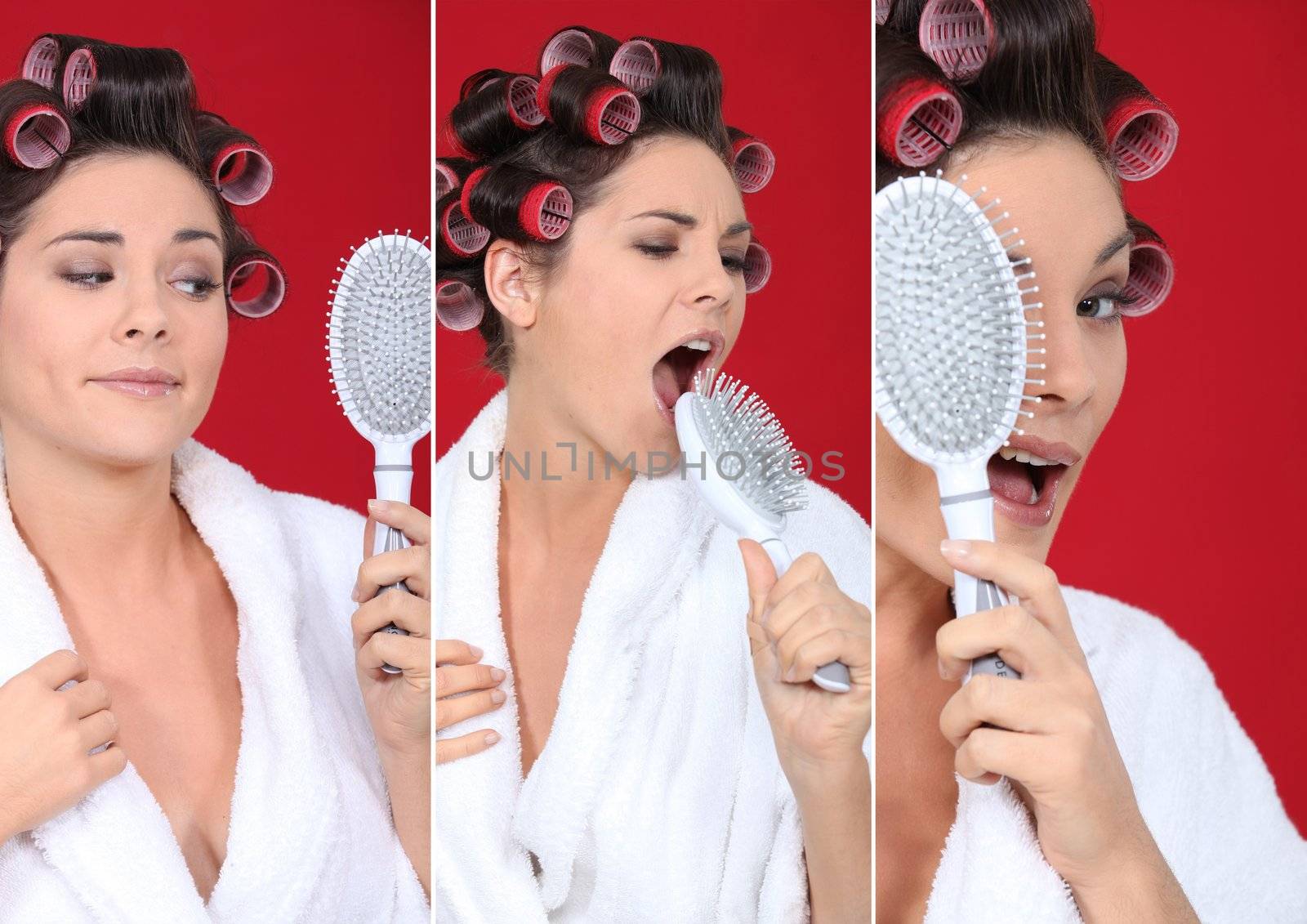 brunette wearing bathrobe with hair curlers holding hairbrush holding against red background