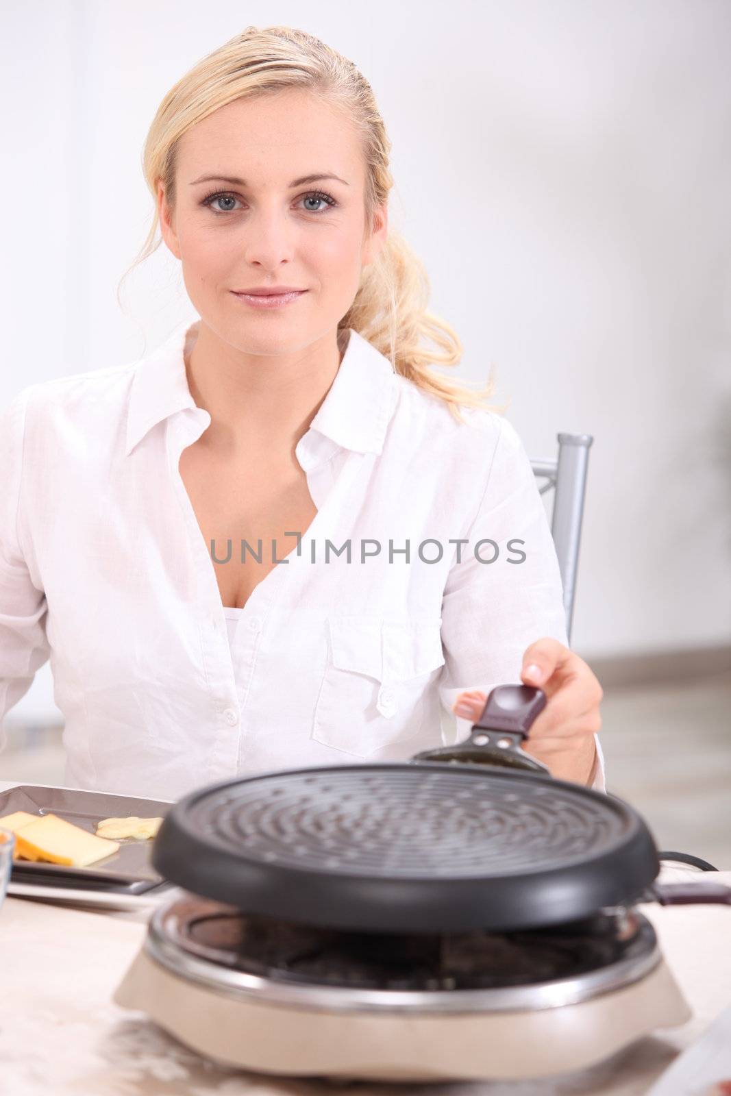 blonde woman in front of a heater preparing melted cheese, potatoes and cold meat (raclette) by phovoir