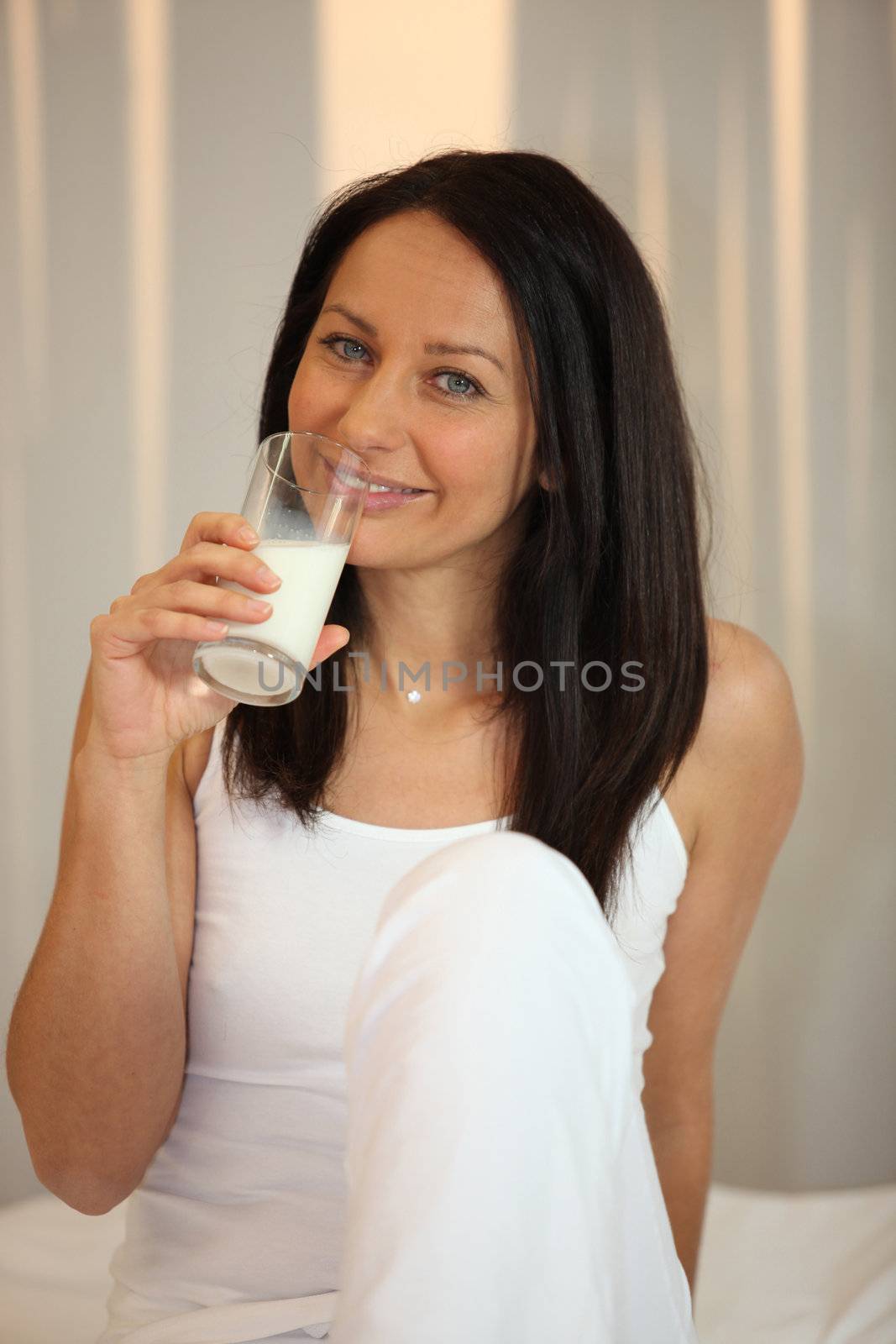 Woman in white drinking a glass of milk by phovoir