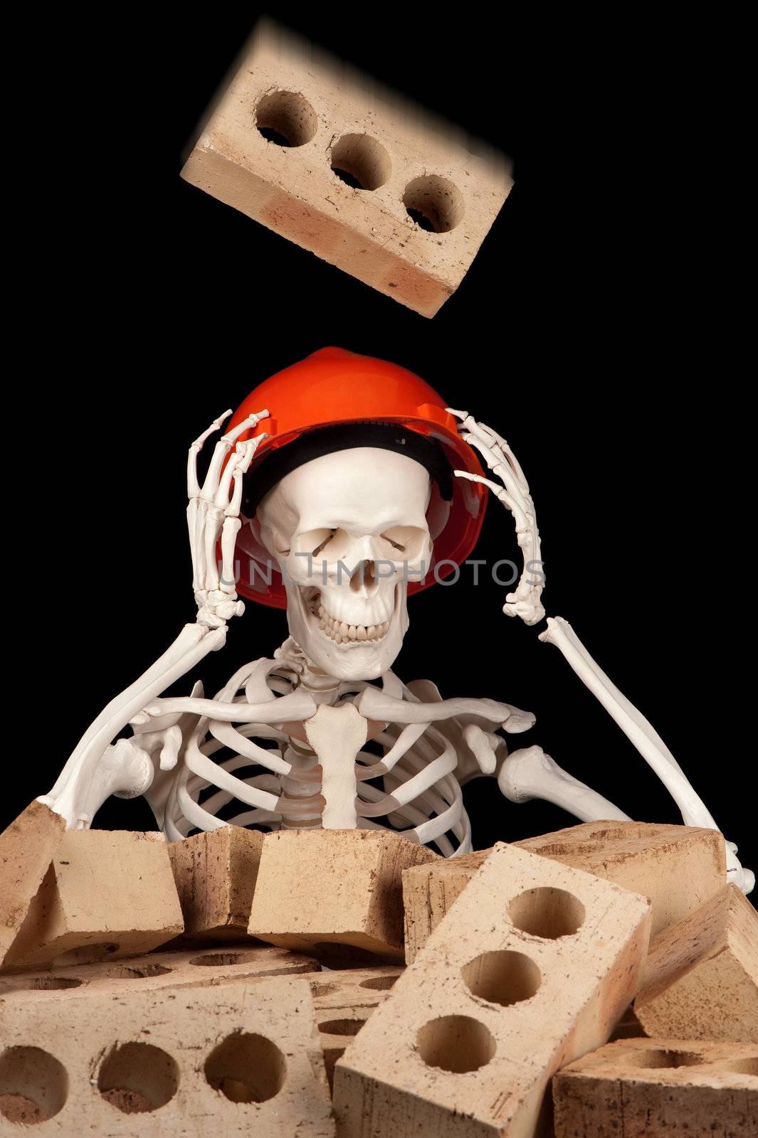 A falling brick is about to make contact with a hard hat on the skull of a skeleton.