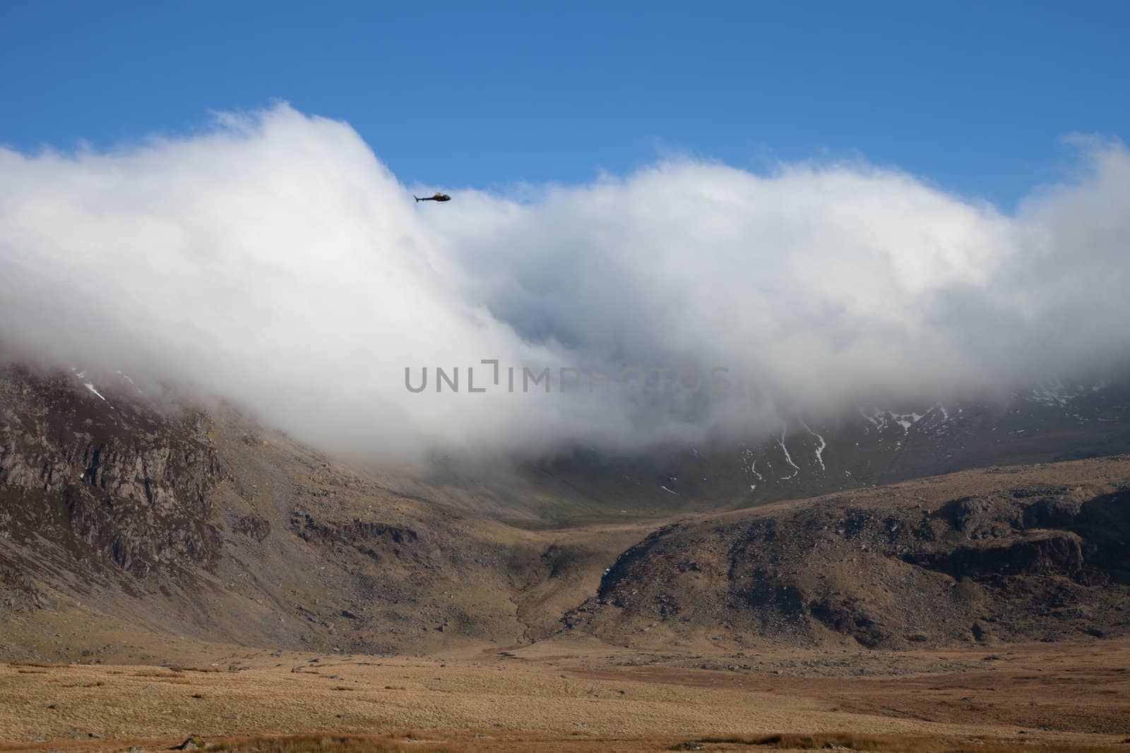 A helecopter patrols over a developing cloud inversion over a mountain peak.