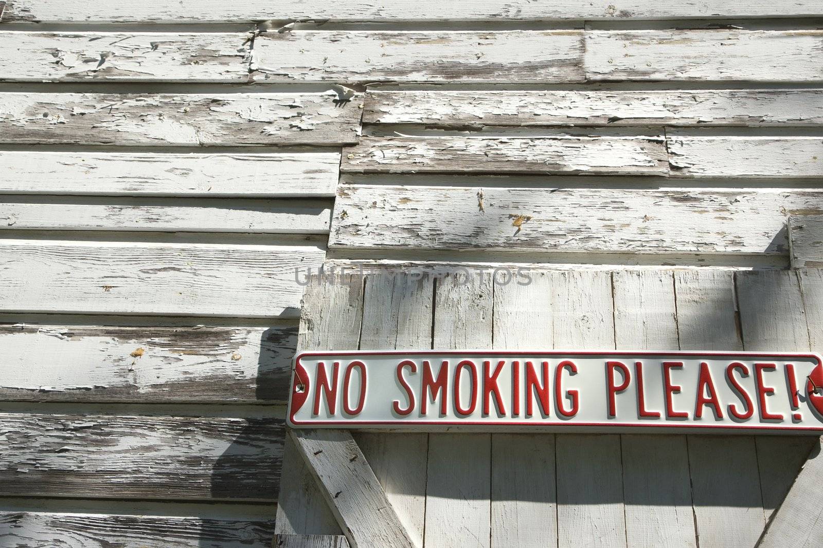 Sign on old white peeling building reading "No smoking please!".