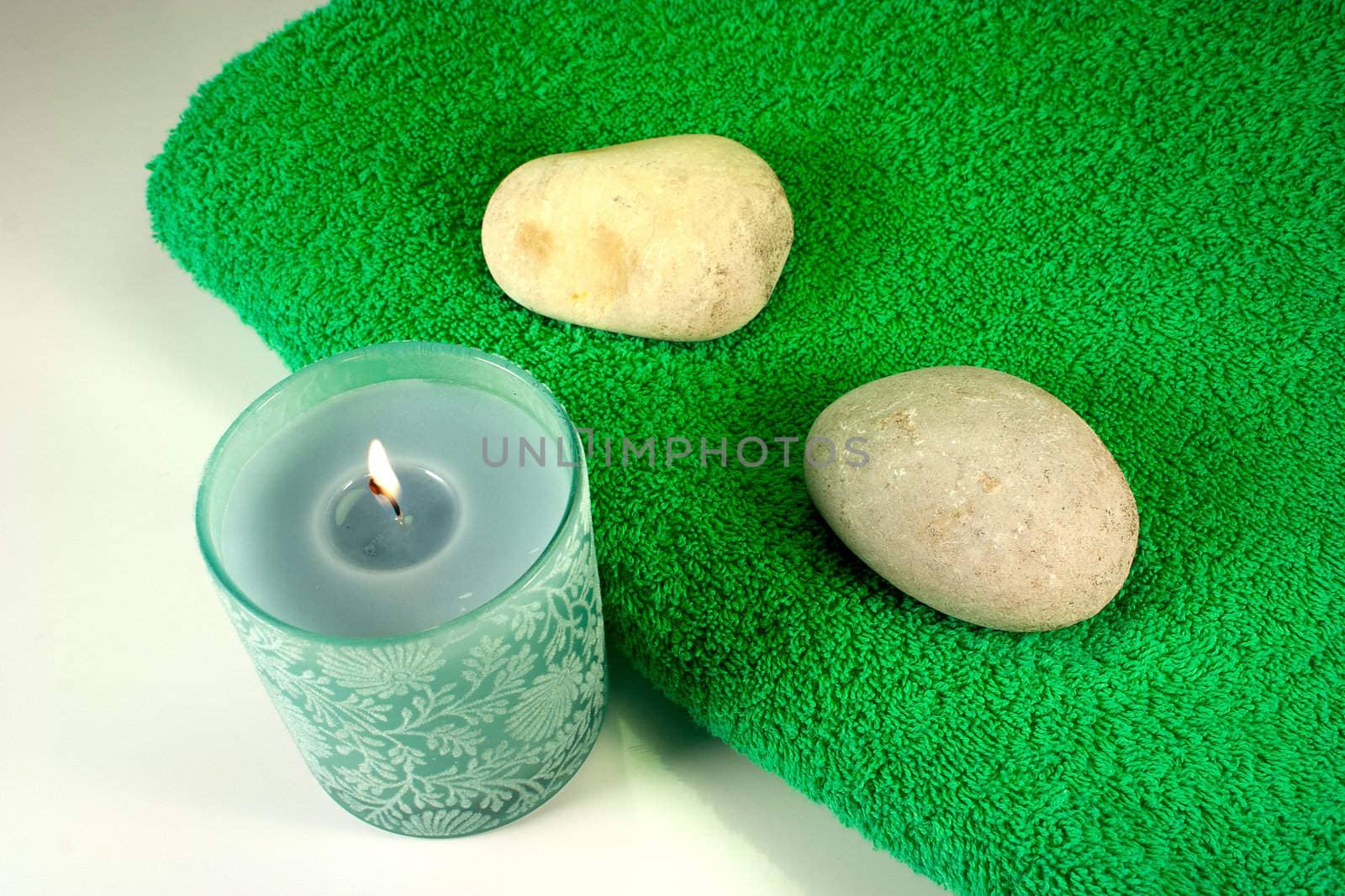 Green candle and stones on green towel
