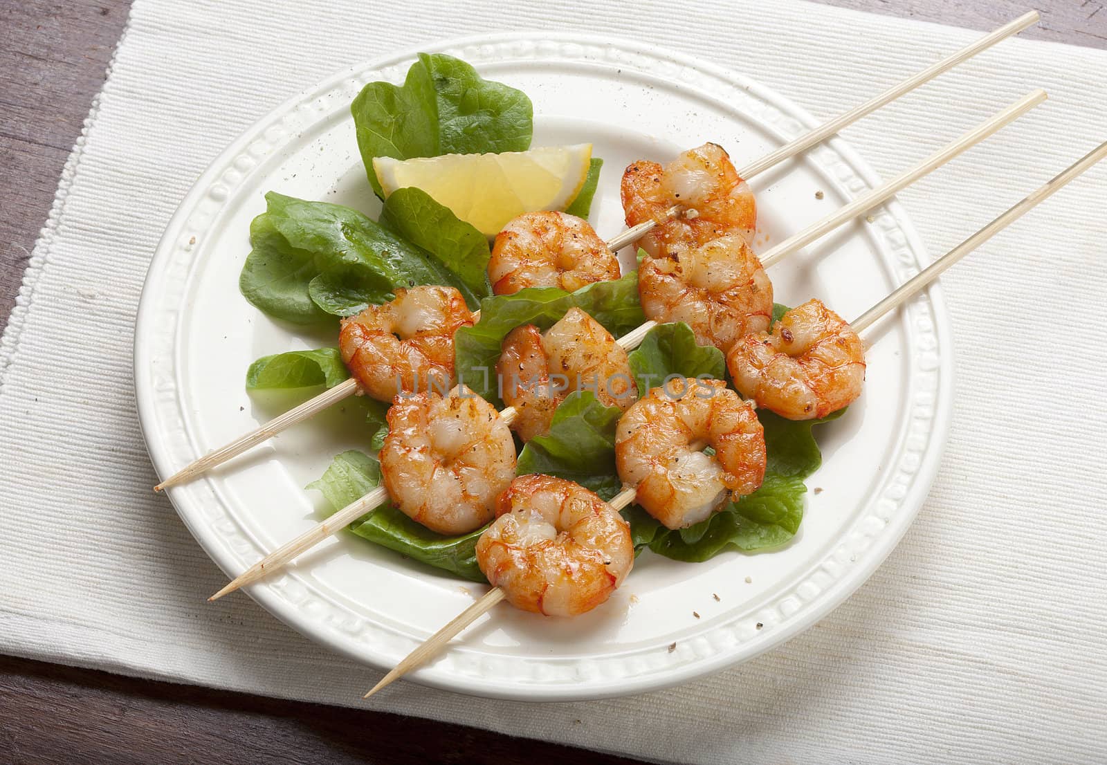 Roasted shrimps on the skewers with lettuce and lemon on the white plate