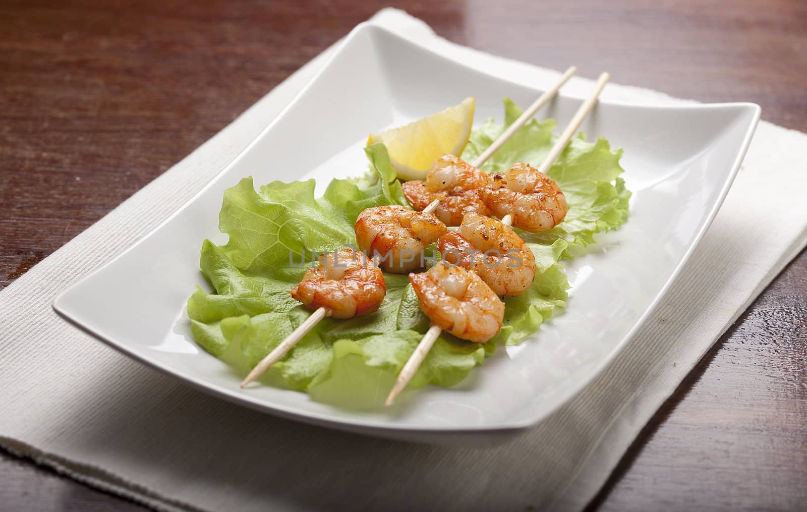 Roasted shrimps on the scewers with lettuce and lemon on the white plate