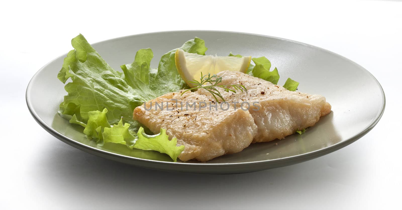 Fried fillet of pangasius with lettuce and lemon on the white plate