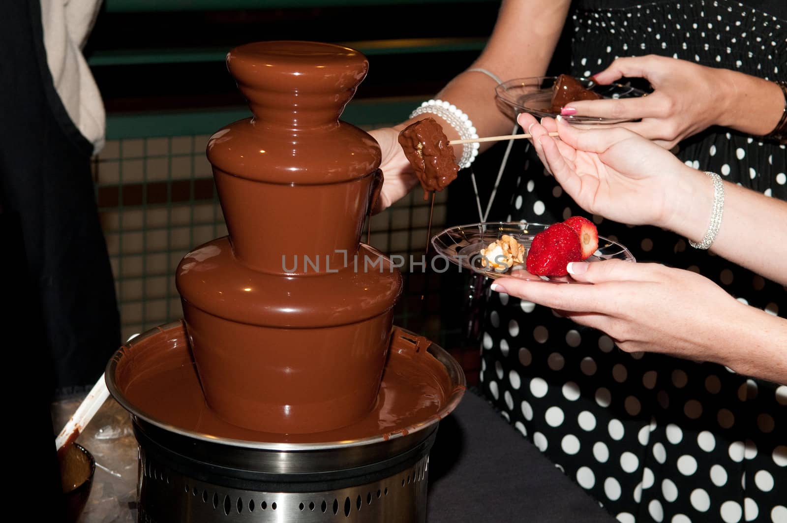 Chocolate fountain with ladies hands dipping their treats at a wedding.