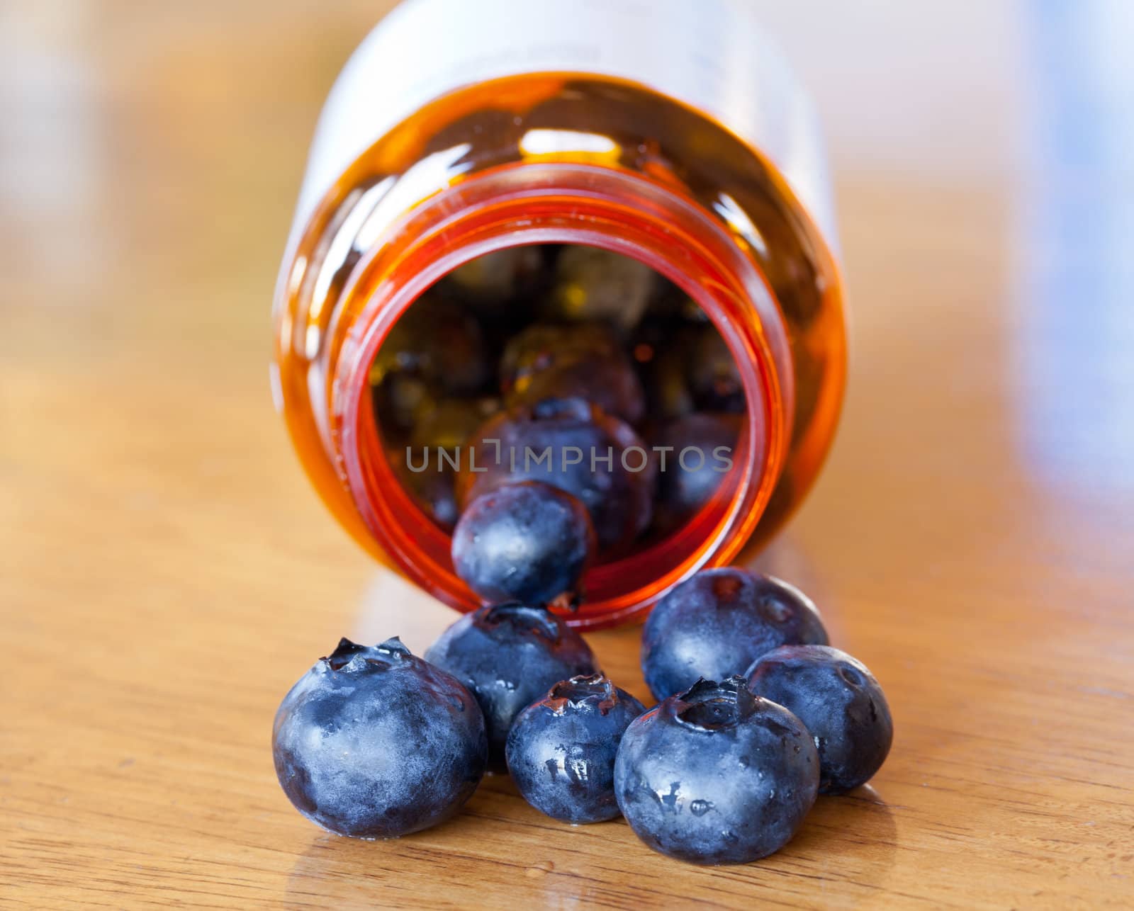 Fresh blueberries being poured from orange prescription bottle onto wooden table for breakfast