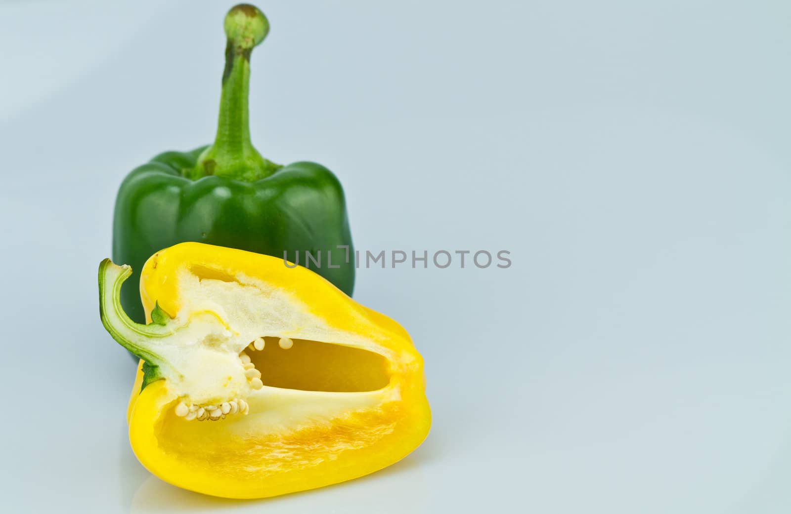 The green whole capsicum and cut yellow capsicum on bluish background