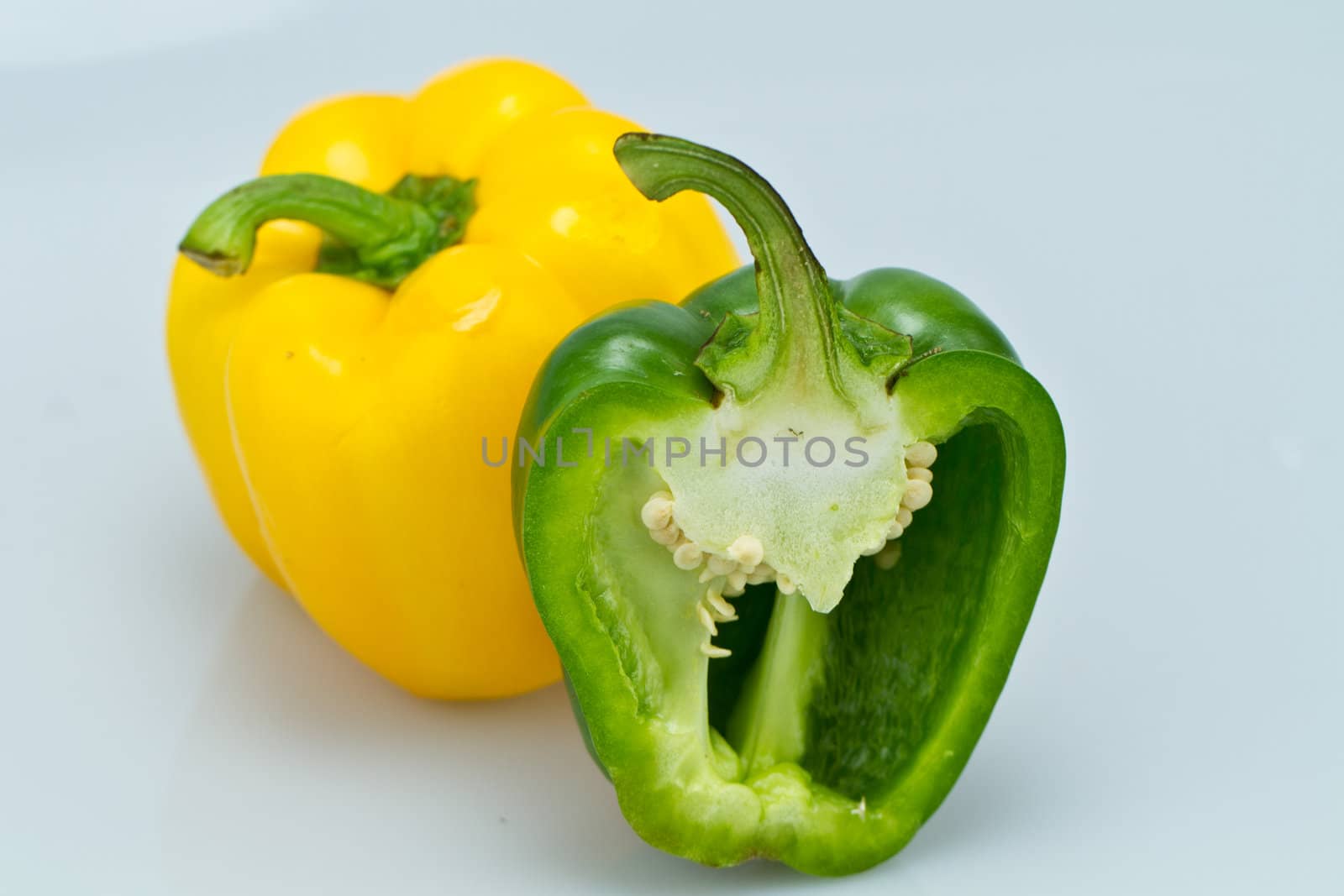 The yellow whole capsicum and cut green capsicum on bluish background