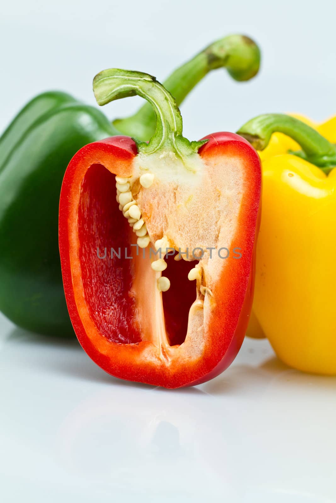 The green and Yellow whole capsicums and a cut red capsicum on bluish background close up view in portrait orientation