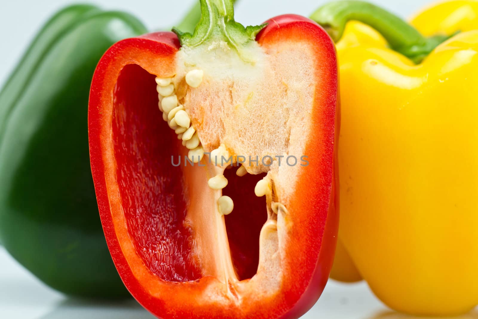 The green and Yellow whole capsicums and a cut red capsicum on bluish background close up view