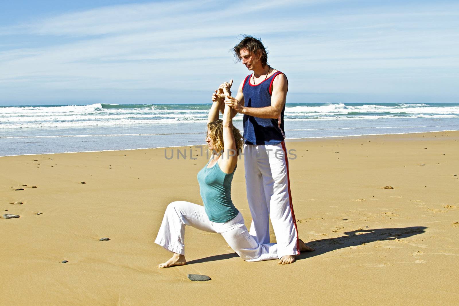 Yoga teacher teaches student yoga on the beach by devy