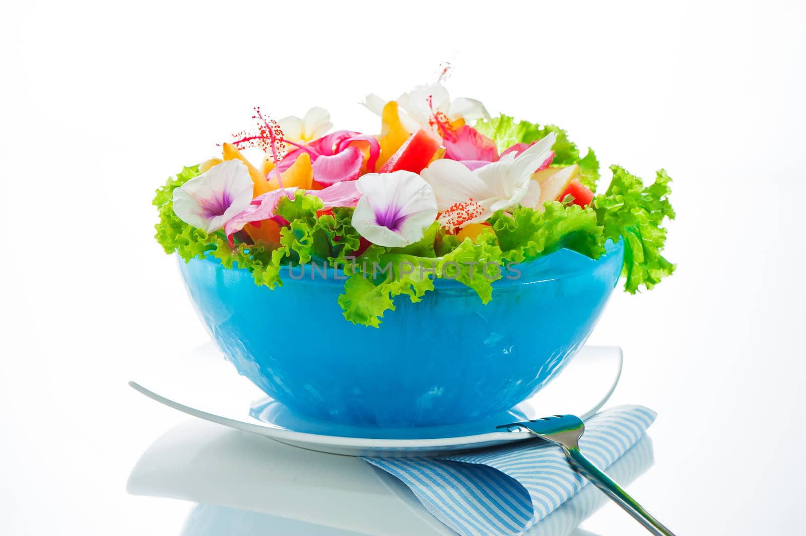 Fruit salad with edible flowers in a blue bowl from ice on white background