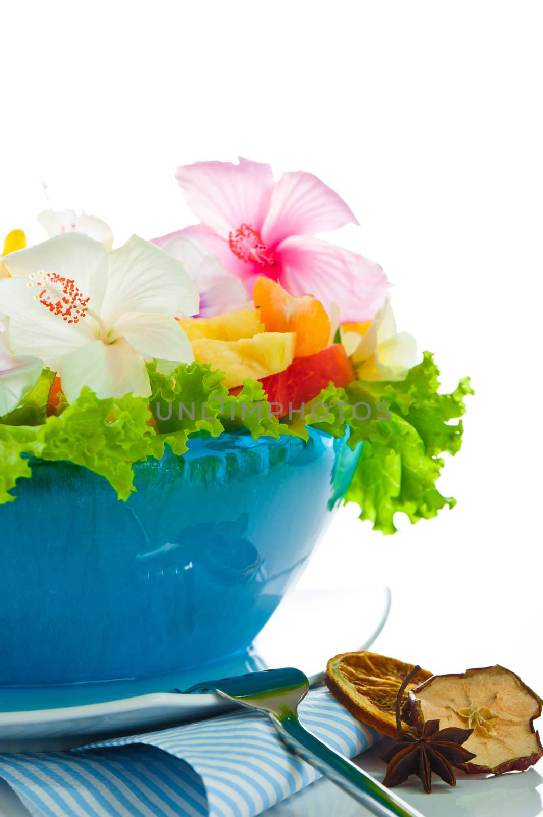 Fruit salad with edible flowers in a blue bowl from ice on white background