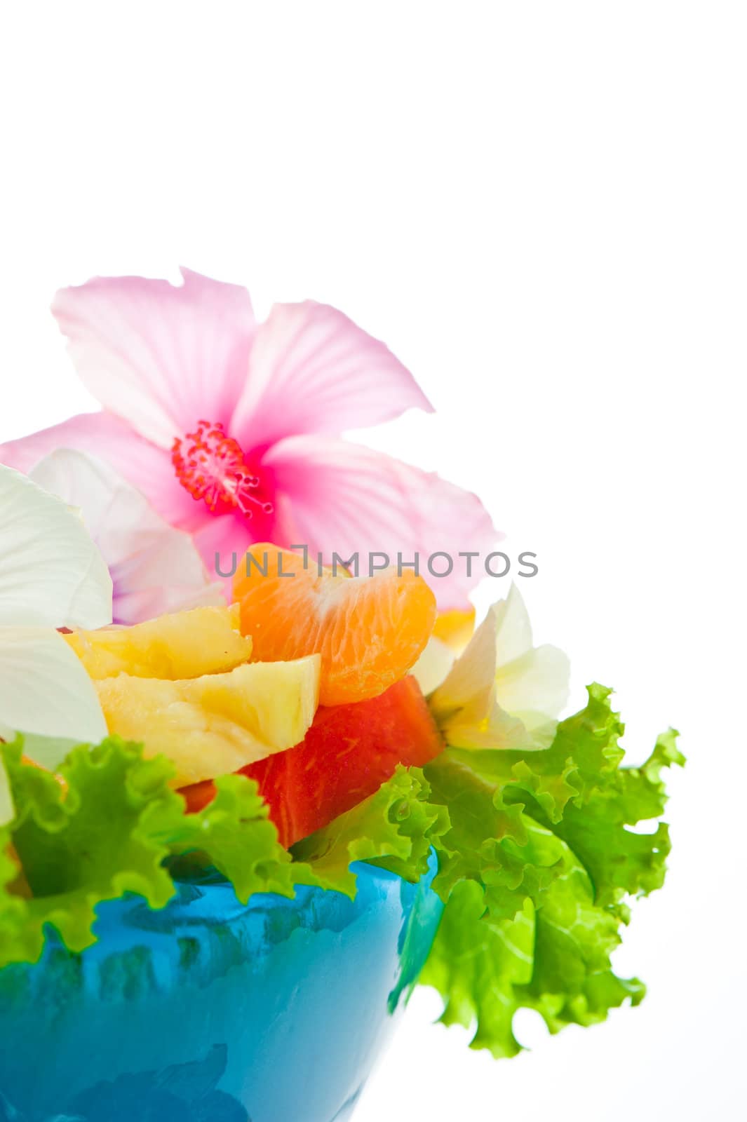 Fruit salad with edible flowers in a blue bowl from ice on white background