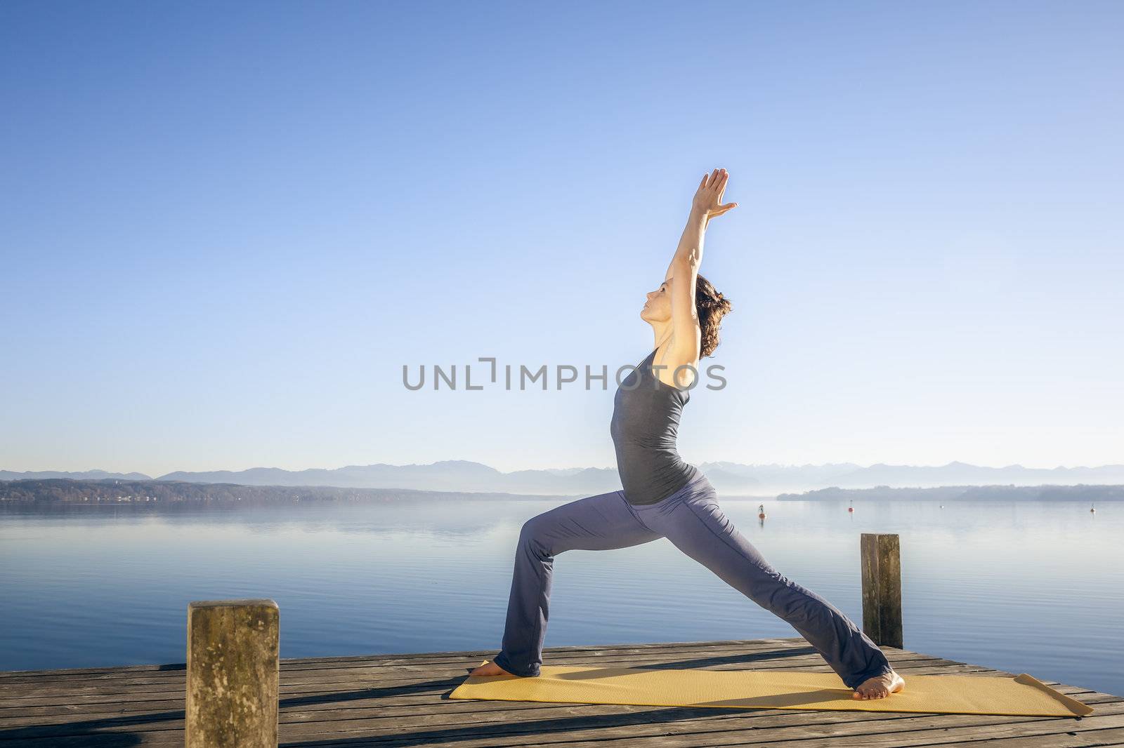 An image of a pretty woman doing yoga at the lake - Virabhadrasana