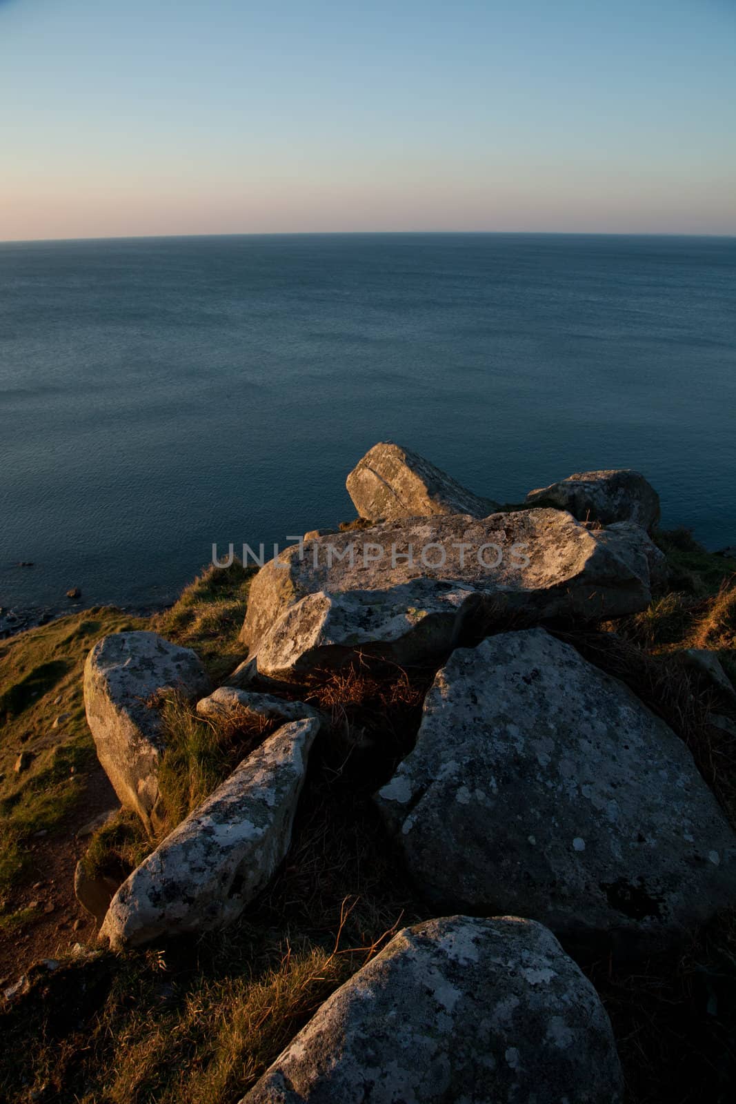 A pile of rocks on the coast in the red evening light and a view of the sea beyond.