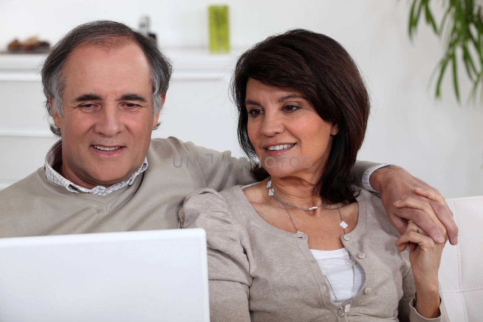 mature couple sitting on sofa with laptop by phovoir