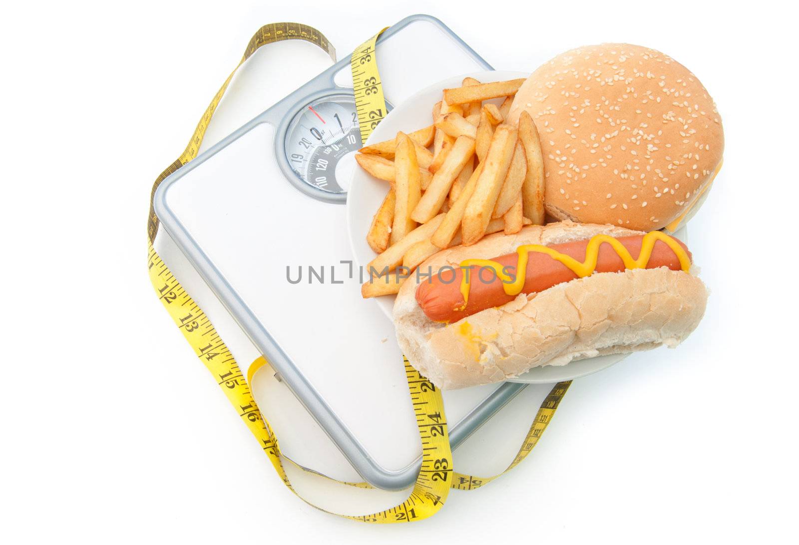 Fattening foods on weighing scales with a tape measure, including burger chips and hot dog