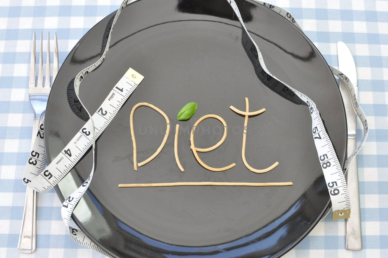 The word diet written with spaghetti on a plate with a measuring tape  
