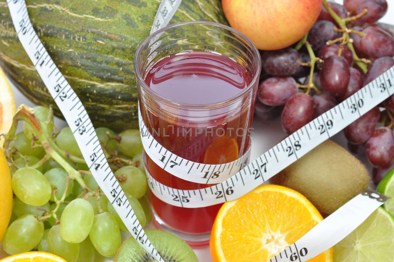 Various fruits around a glass of juice and a tape measure  