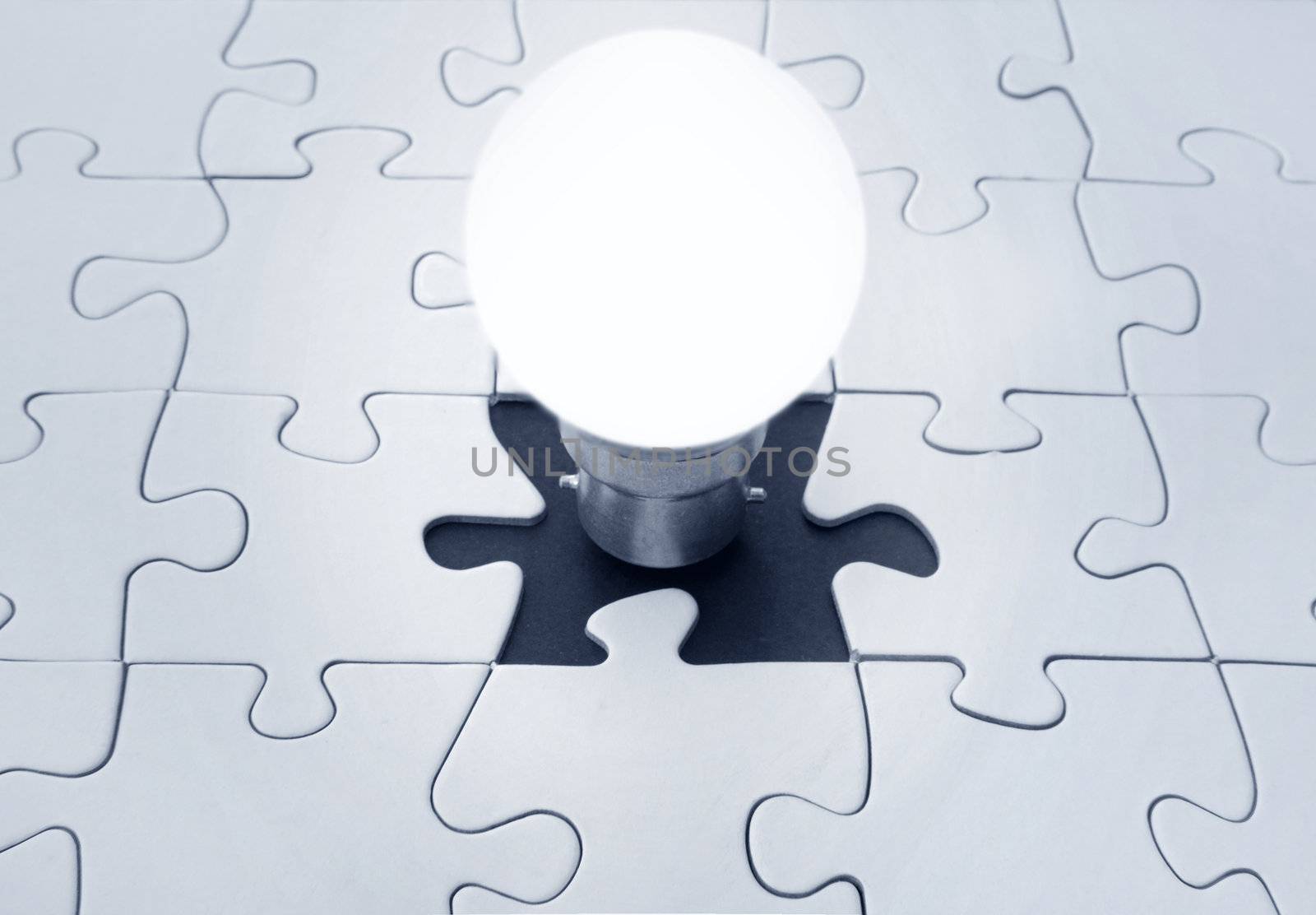 Light bulb emerging from the missing piece of a jigsaw puzzle. A conceptual image which represents such themes as solutions, ideas, inspiration and brainstorming. 