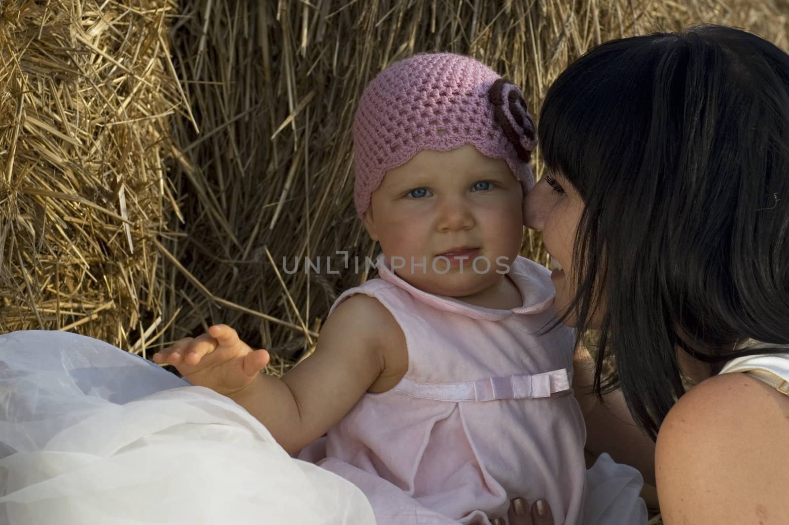 Little baby girl is sitting on hay, her mother is looking on her