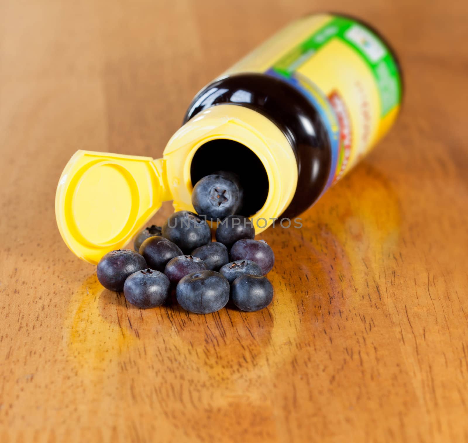 Fresh blueberries being poured from yellow vitamin bottle onto wooden table for breakfast