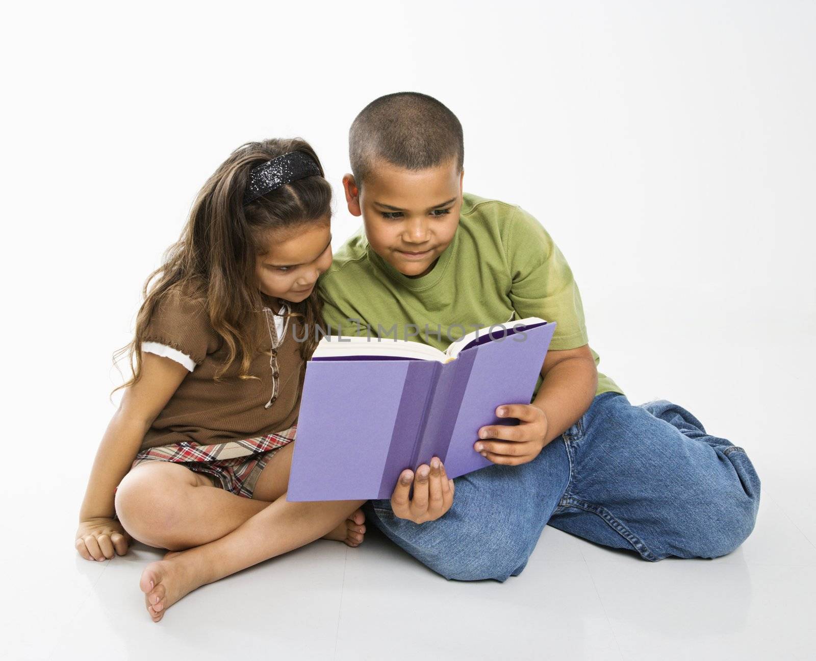 Hispanic brother and sister reading book together.