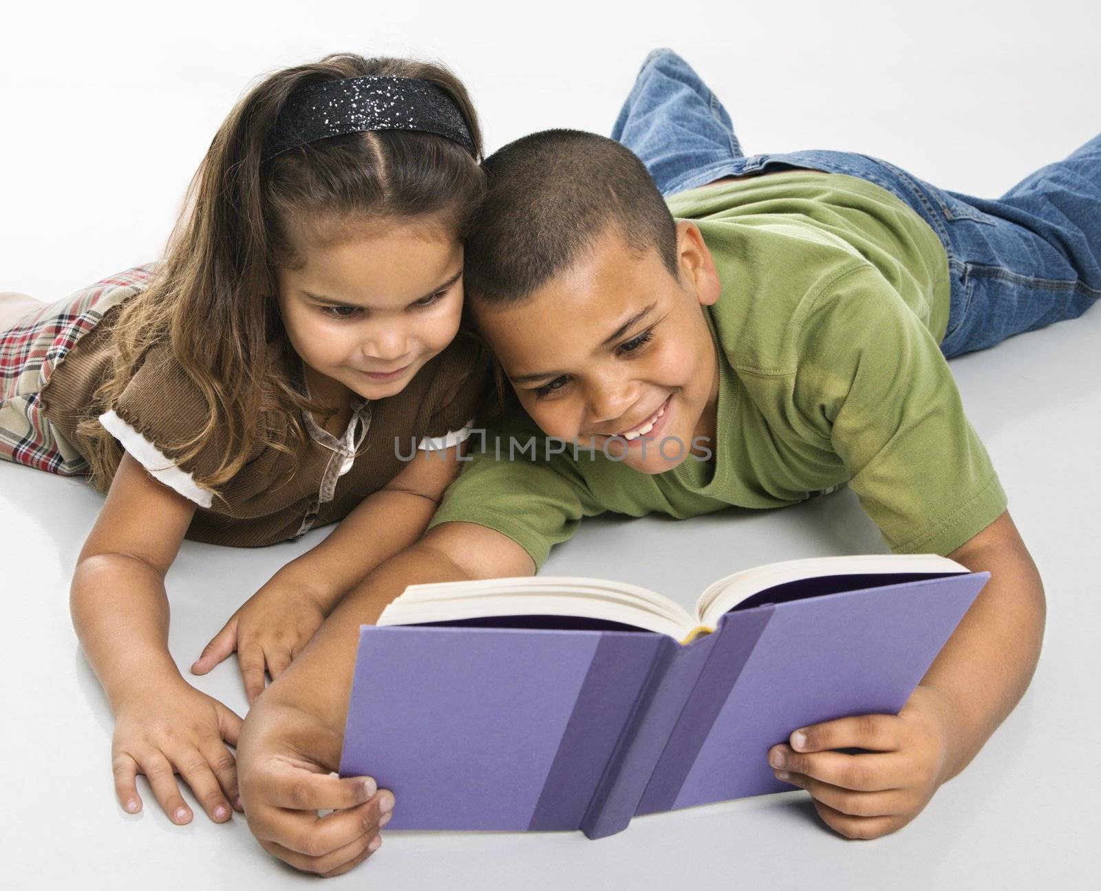 Hispanic brother and sister reading book together sitting on floor.