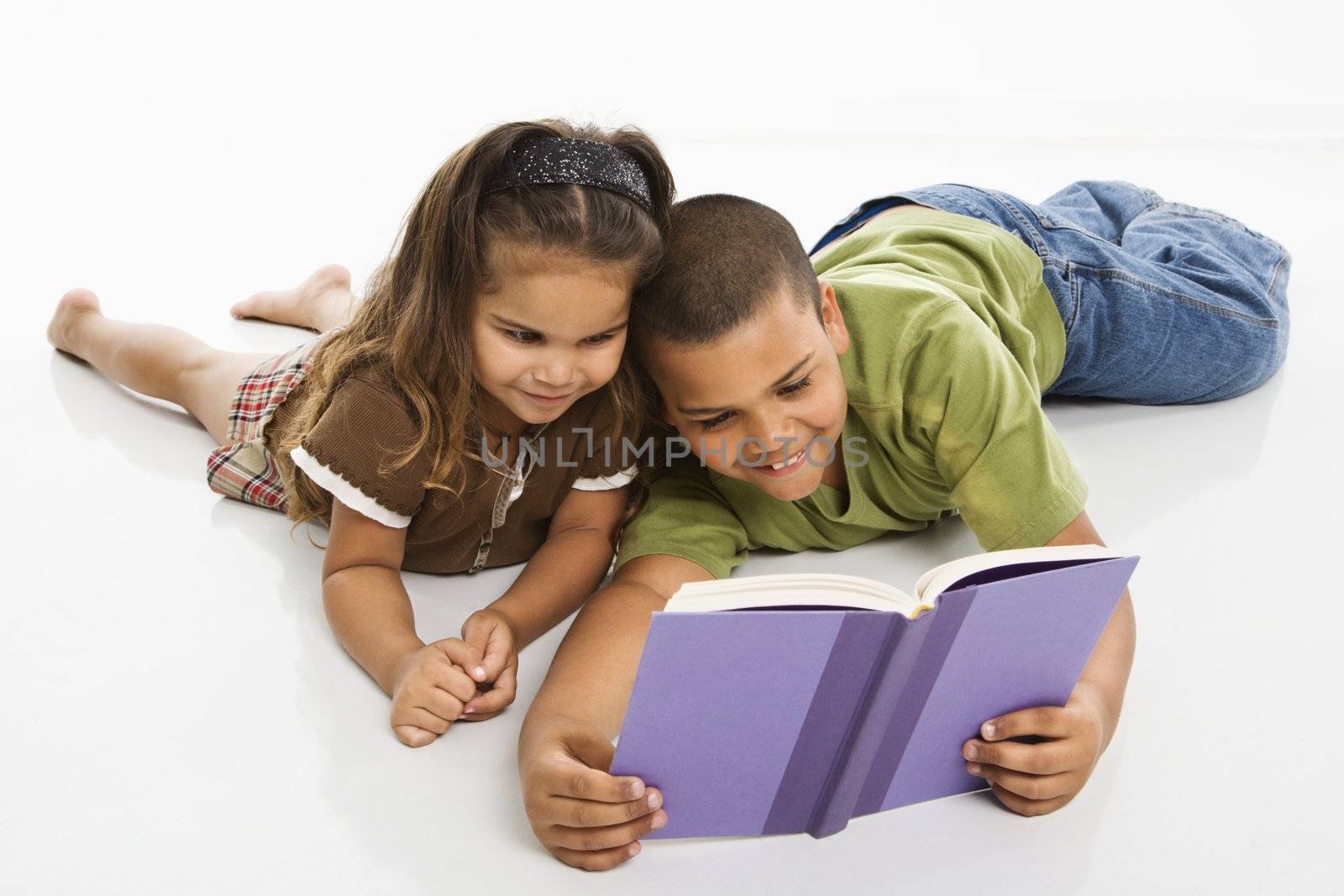 Hispanic brother and sister reading book together.