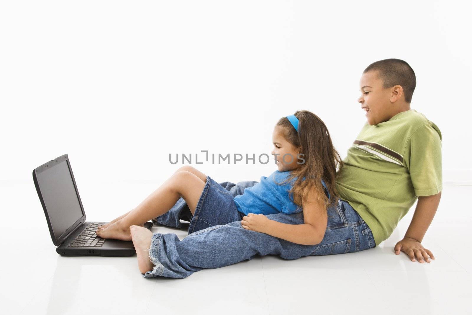 Brother and sister putting feet on laptop computer and smiling.