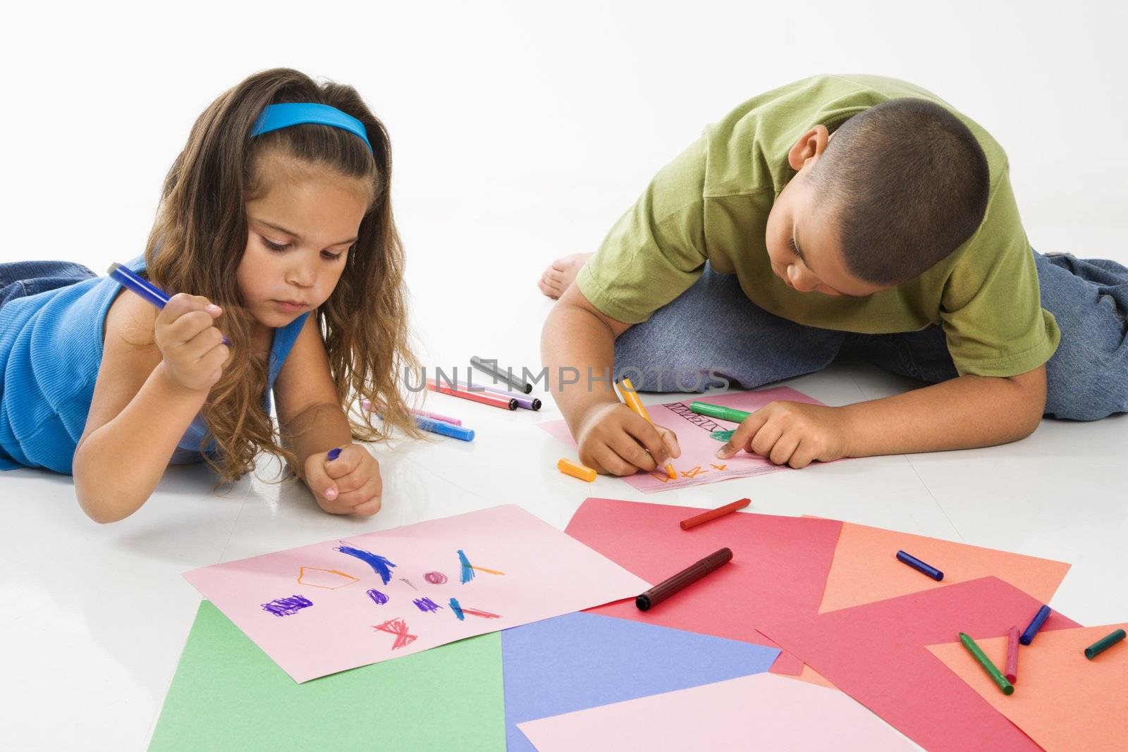 Young latino boy and girl coloring on construction paper and smiling.