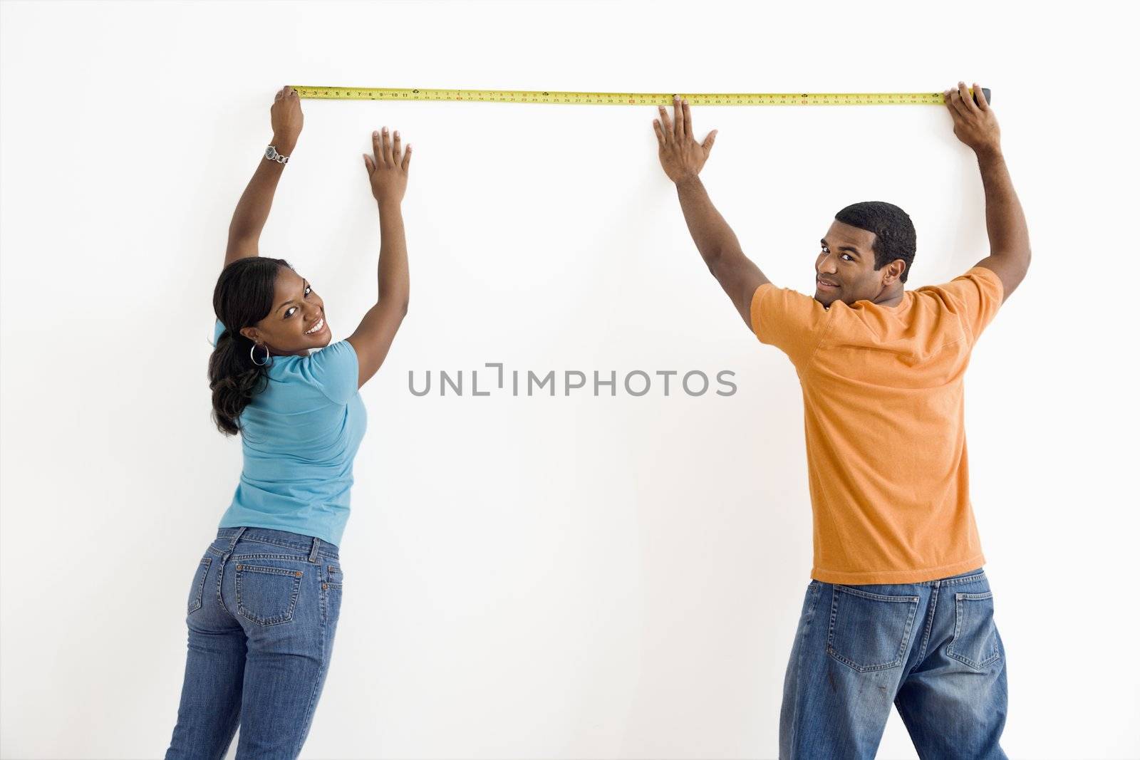 African American male and female measuring wall and looking at viewer.