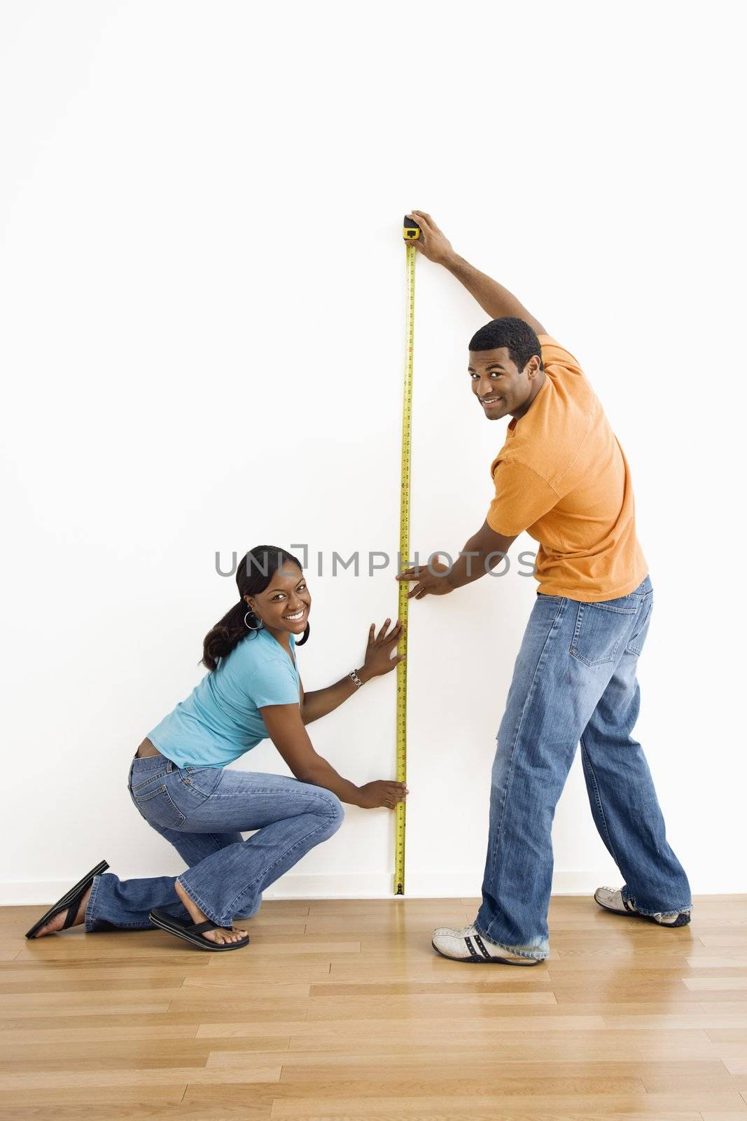 African American male and female measuring wall and looking at viewer.