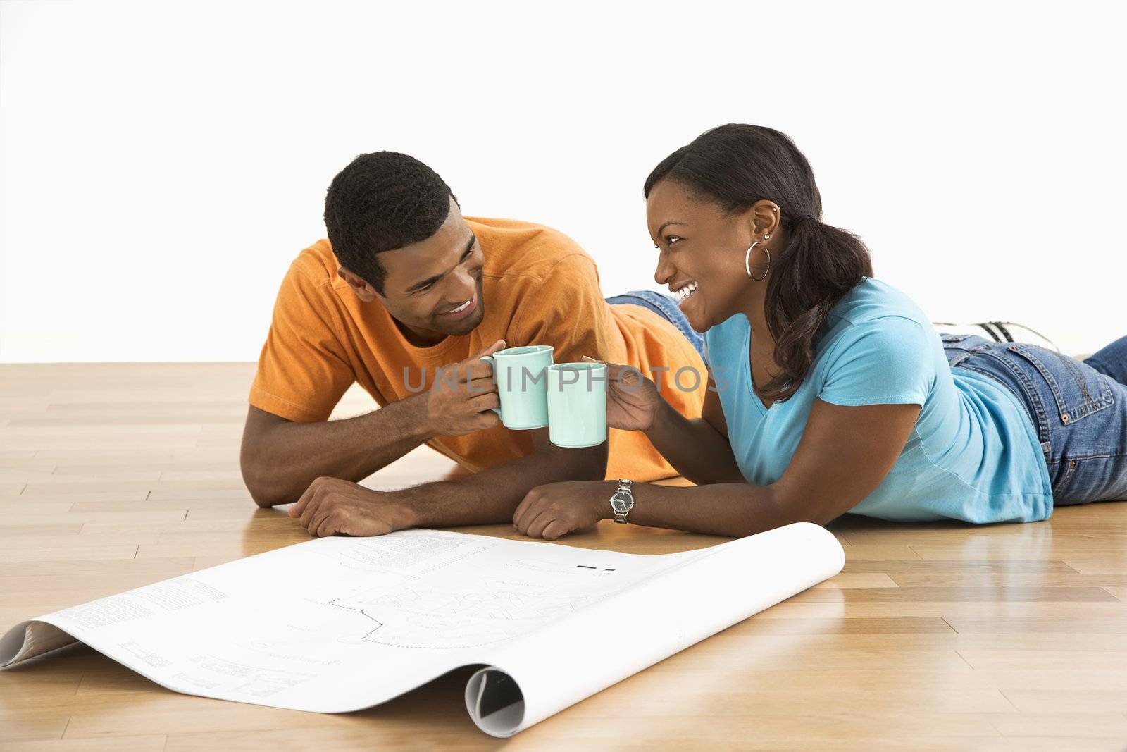 African American male and female couple with architectural blueprints toasting with their coffee cups.