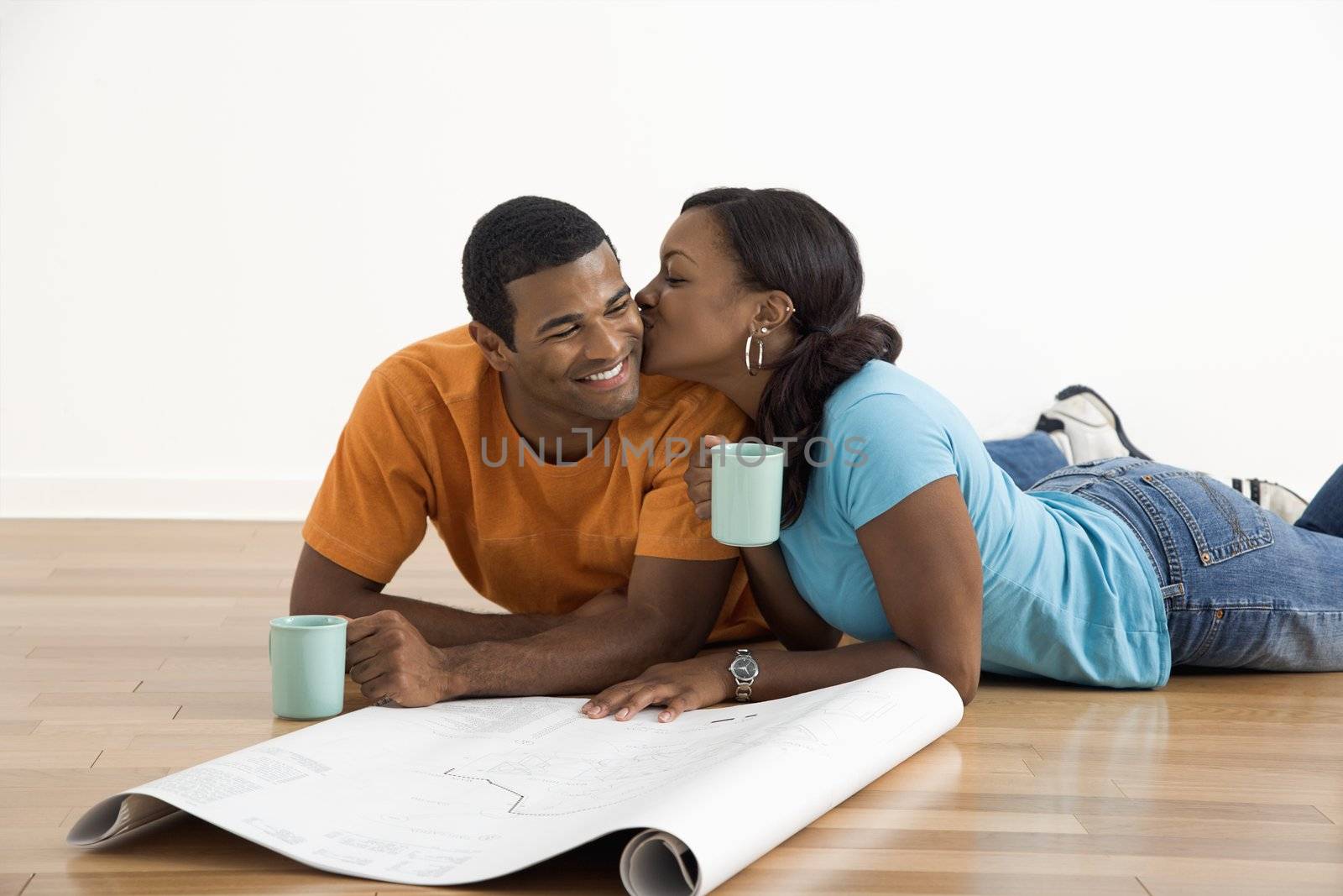 African American female kissing man next to blueprints.