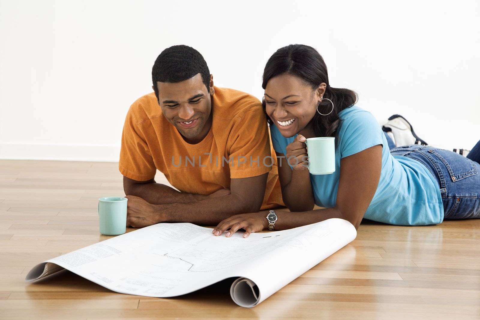 African American male and female couple lying on floor looking at architectural blueprints.