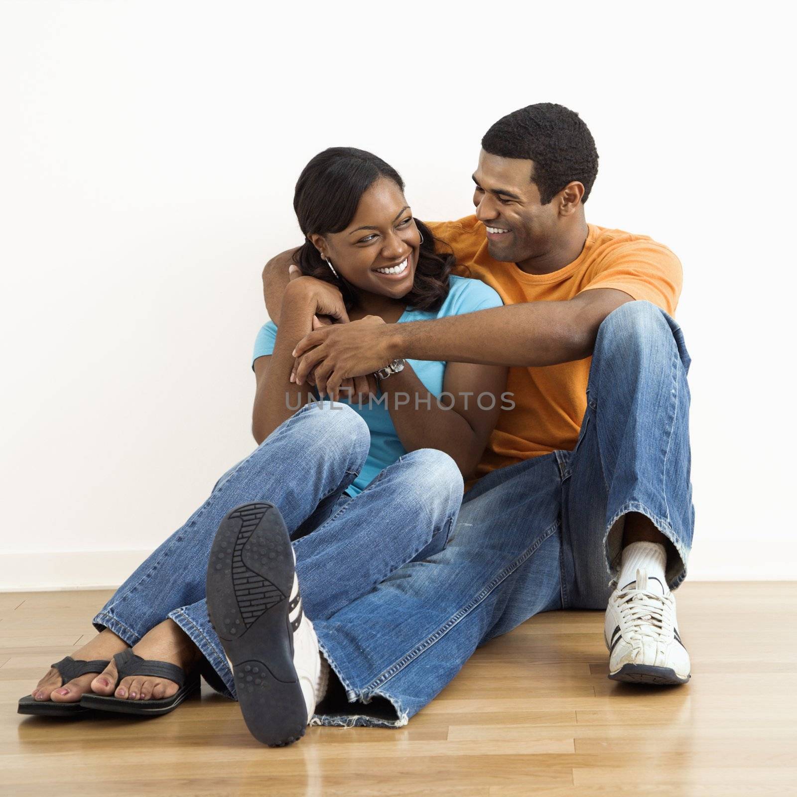 Happy, smiling African American couple sitting on floor snuggling.