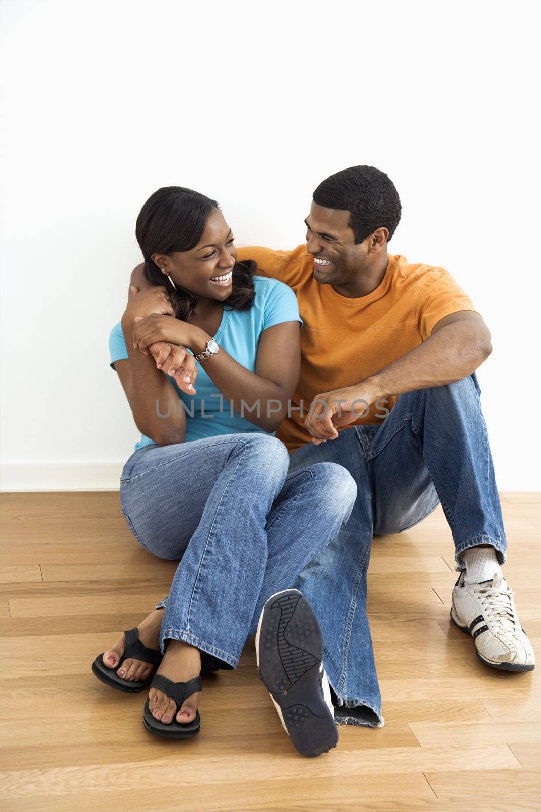 African American male and female couple sitting on floor relaxing and laughing.