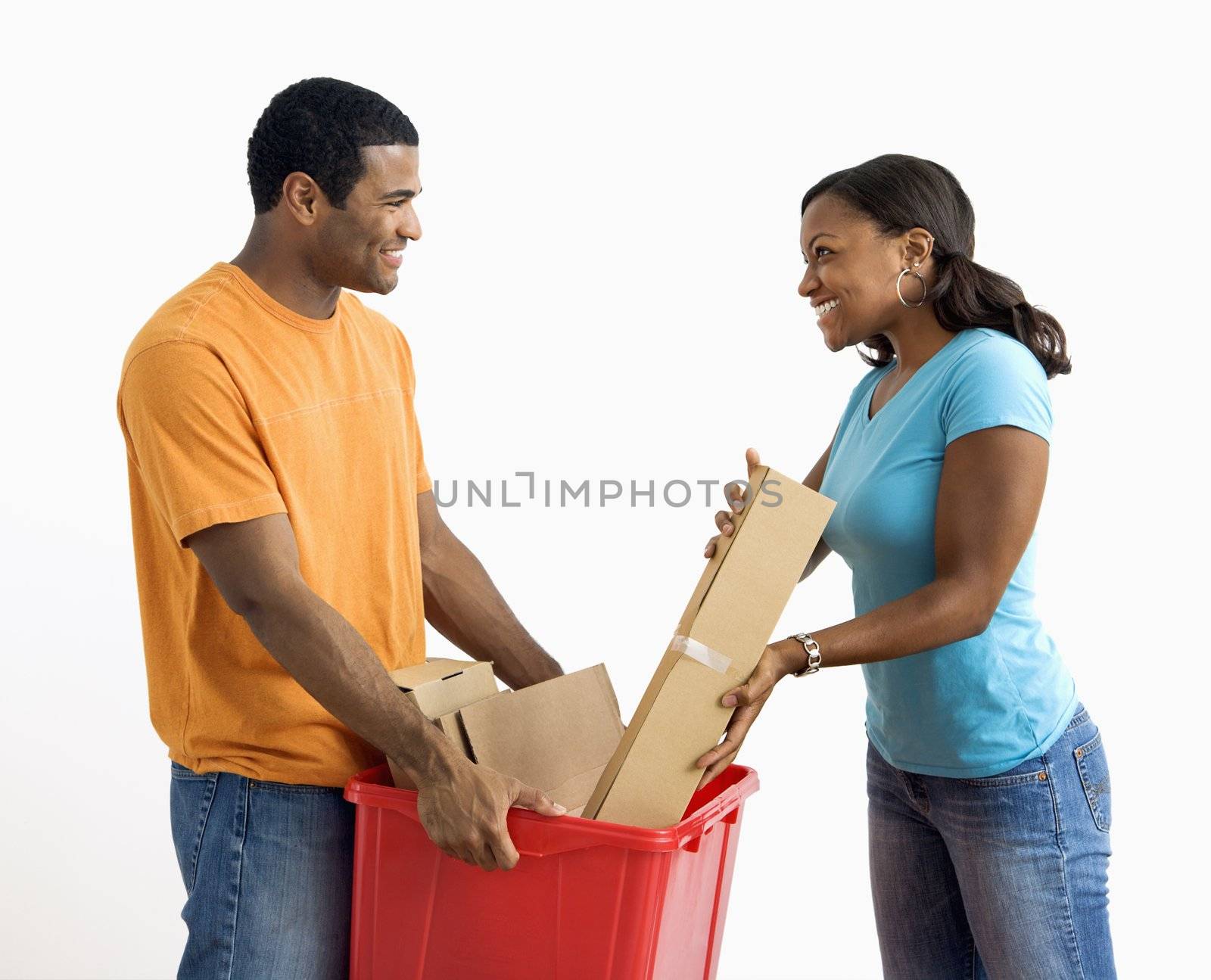 African American male holding recycling bin while pretty female puts cardboard in.