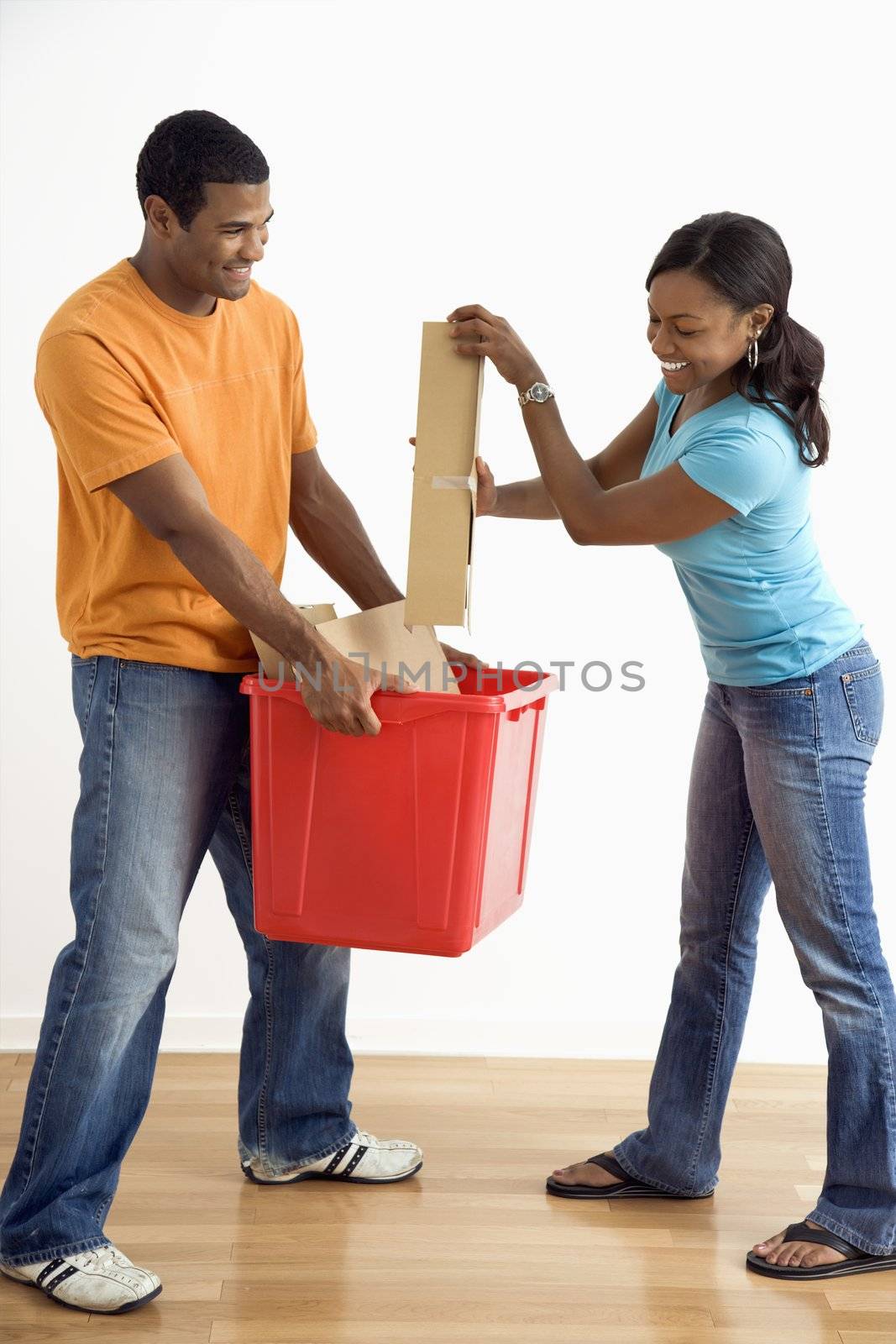 African American male holding recycling bin while pretty female puts cardboard in.