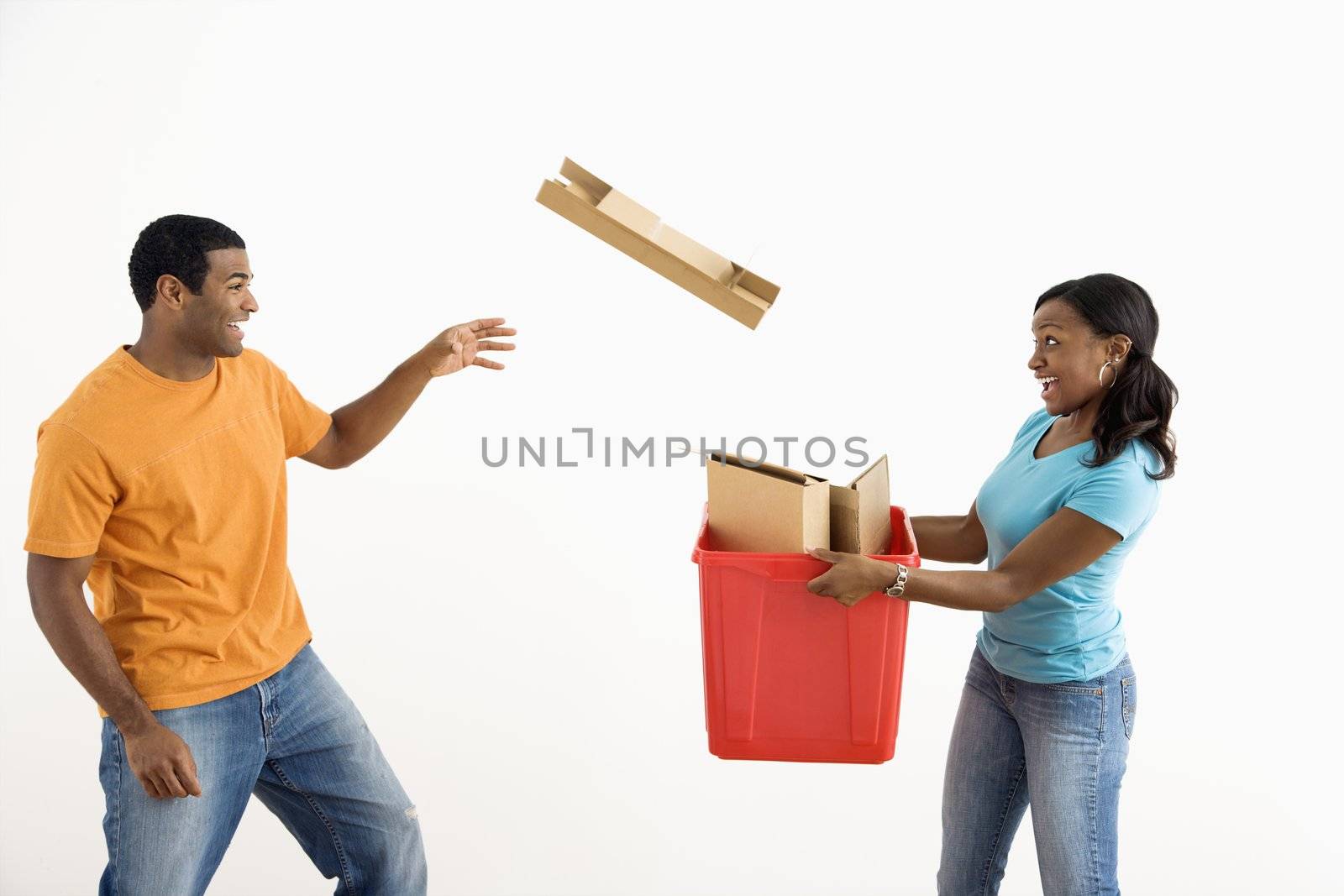 African American female holding recycling bin while male tosses cardboard into it.