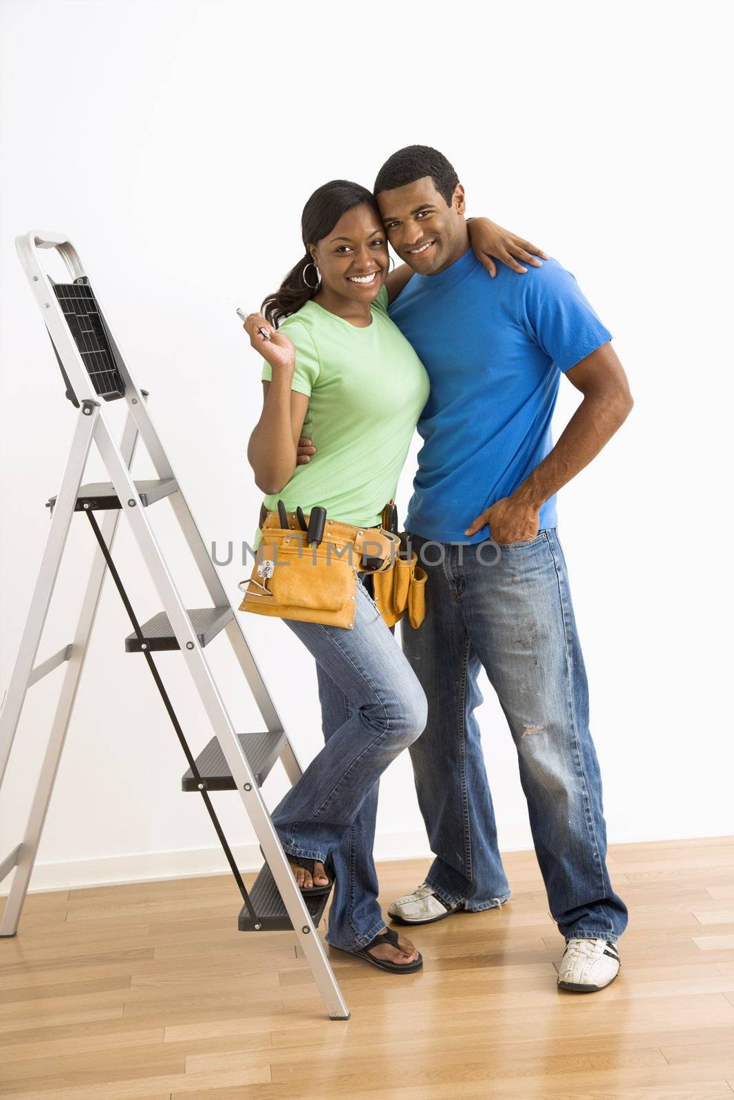 Portrait of smiling African American male and female couple with home repair tools and ladder.