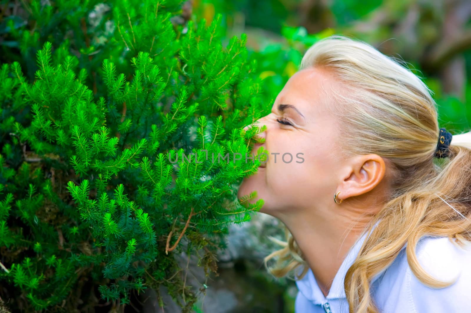 Funny blond girl smelling the green bushes